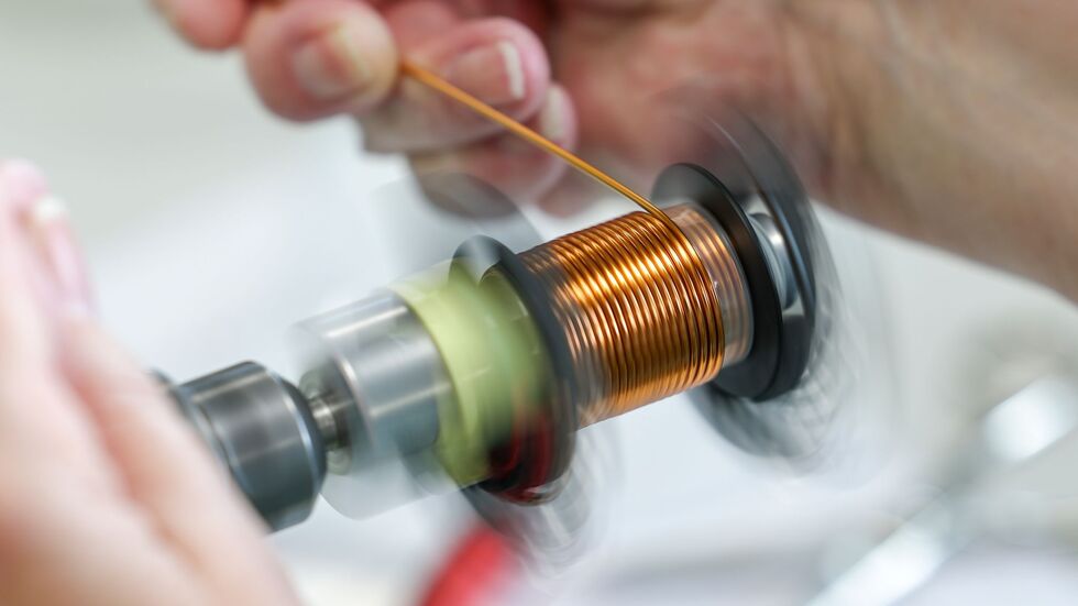 An einer Maschine wickelt eine Mitarbeiterin eine Spule für eine PFC-Drossel. 