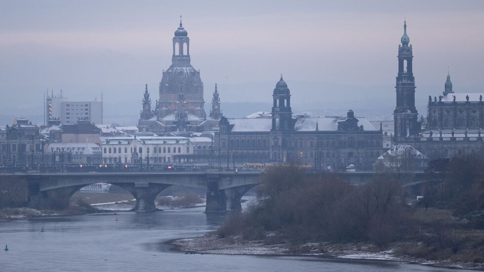 Mit Schnee bedeckt ist die Kuppel der Frauenkirche bei Sonnenaufgang.